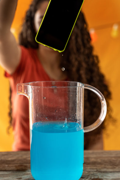 一名年轻女子将智能手机扔进了一罐蓝色鸡尾酒中图片下载