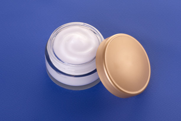 玻璃罐与身体霜和金色帽附近的蓝色背景。用于皮肤护理的化妆品。图片下载