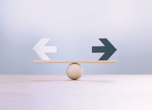 在离焦背景前，白色和黑色木制箭头坐在木制跷跷板上图片下载