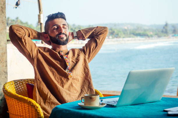 迷人的埃及男员工在有海洋背景的自助餐厅使用电脑图片下载