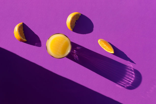 橙汁和橙片在深紫色的背景上有长长的阴影。图片下载