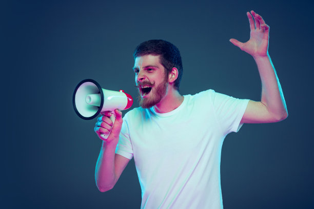 有人对着扩音器大喊。英俊的白人男子的肖像孤立在深蓝色的工作室背景。图片下载