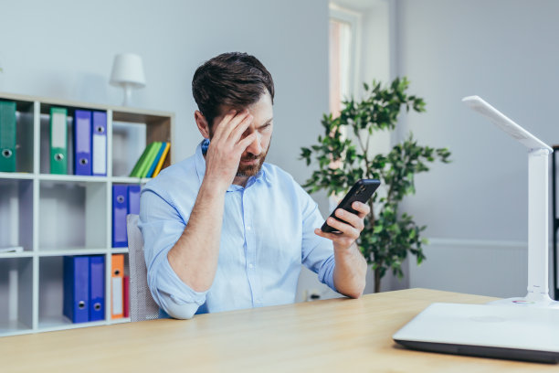 沮丧和悲伤的商人看着手机屏幕，男人在明亮的办公室工作图片下载