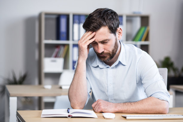 近距离的照片。沮丧、疲惫、有思想的年轻人，办公室职员、经理、自由职业者。他用手抱着头。坐在办公室的电脑桌前图片下载