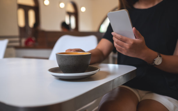 一名年轻女子在咖啡馆喝咖啡时手持和使用手机的特写图像图片下载