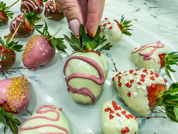 草莓巧克力中。甜甜的甜点，诱人的巧克力浆果。一个做法式美甲的女孩，绿色的马尾辫上拿着一个浆果图片下载