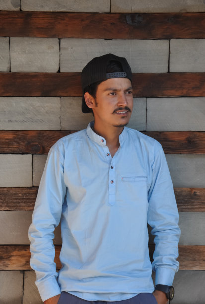 一个印度年轻人戴着帽子向后看，手放在口袋里靠墙摆姿势图片下载