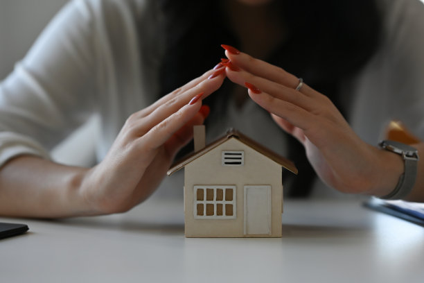 特写：女人的手保护着白色办公桌上的房屋模型，用于住房、金融和房地产业务。图片下载