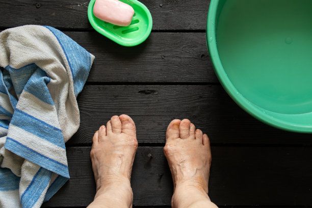 老奶奶在黑色地板上用塑料碗里的水和肥皂洗脚图片下载