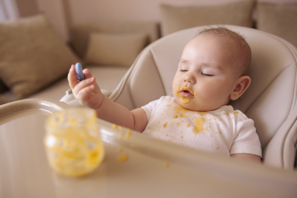 小男孩饭后坐在高脚椅上，拿着脏兮兮的勺子图片下载