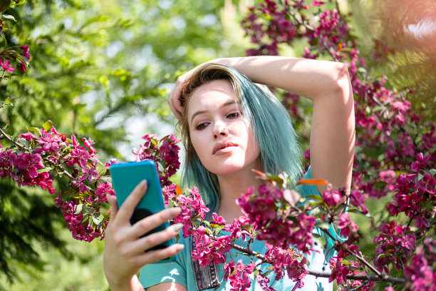 蓝发女子在春花树前自拍。图片下载