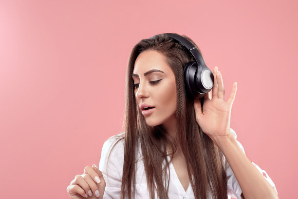 戴着无线耳机在粉色背景上听音乐的女孩图片下载