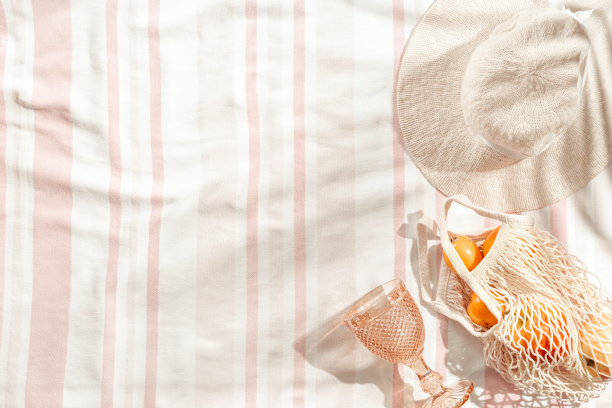 夏天最小平面宽檐帽，彩色酒杯，橙色水果在条纹沙滩毛巾为背景，阳光的阴影。夏天粉彩审美照片图片下载