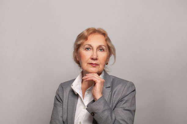 美丽的中年女士微笑着看着灰色背景的相机。60年代成熟女性画像图片下载