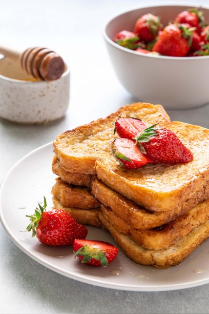在浅色的背景上，铺上草莓和蜂蜜的法式吐司。早餐、早午餐或午餐的概念。有选择性的重点。图片下载