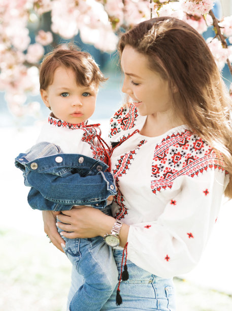 小男孩抱在妈妈的手上。在春天盛开的花园里，女人和孩子在外面玩耍。两个人的家庭肖像。春天风景背景。图片下载