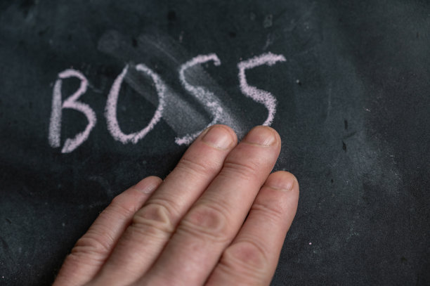 黑色黑板上半擦去的“BOSS”字。一名成年男子的左手用手指擦掉了手写的单词。黑色表面模糊的字母。图片下载