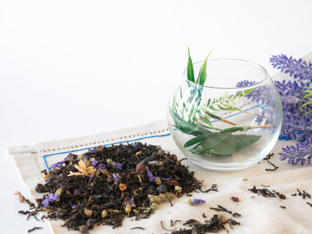 花草茶，蓝色干花装在圆玻璃花瓶里，茶水散落在桌子上和亚麻餐巾上。薰衣草花图片下载