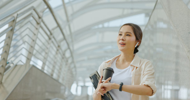 亚洲女商人在上班的路上用蓝牙耳机开会，脸上带着幸福的微笑。妇女使用城市交通路线免费的互联网技术在城市图片下载