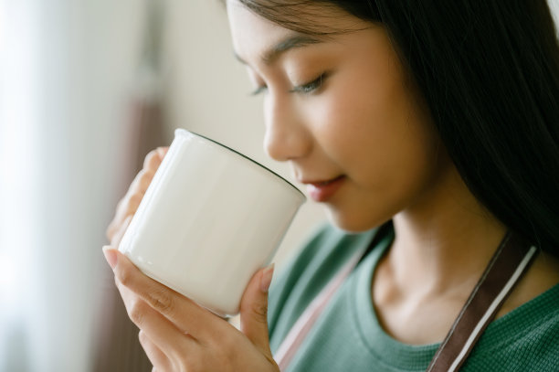 清晨，年轻亚洲女人在家中厨房窗边手捧马克杯喝牛奶图片下载