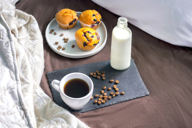 床上放着装有咖啡和牛奶的黑色托盘，早餐放着松饼。在家安全隔离概念与拷贝空间图片下载