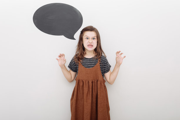 女孩秀出吓人的表情。白色背景下小女孩穿着万圣节服装的搞笑动作。模拟墙上的文字。图片下载