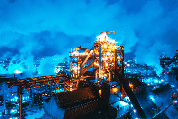 鸟瞰冶金厂高炉的夜晚，烟囱和火焰从管道中燃烧。具有冶金生产高炉的工业全景地标图片下载