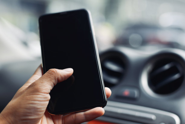 特写男性手握和使用现代智能手机在汽车之间的交通堵塞，空白屏幕为您的内容或短信。图片下载