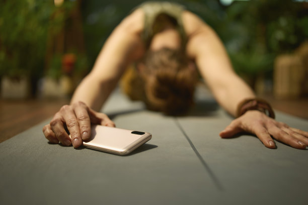 时尚的女人在绿色的客厅做瑜伽和使用电话图片下载