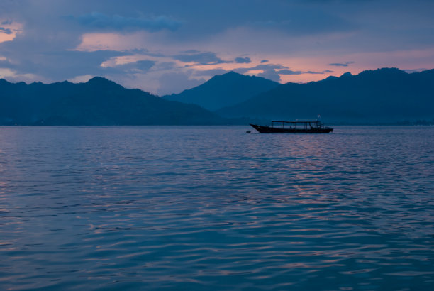 五彩斑斓的热带海洋景观在日落与蓝色的山在雾霾，平静的大海和传统的印尼渔船在粉红色的太阳在光滑的水面上闪耀。风景秀丽的大海，旅游亚洲。图片下载