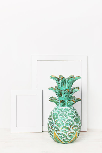 一张照片的木制空框和白墙背景上的一个木制祖母绿菠萝。空白纸框架，现代家居装饰模型。室内背景。图片下载