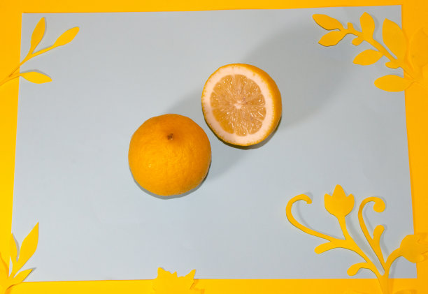 将柠檬对半切在灰色纸上，边缘以黄色为底色，黄色纸花，创意现代设计，健康食品，夏天，维生素图片下载