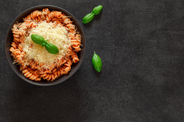 用番茄酱、罗勒和磨碎的帕尔马干酪烹制的意大利面，黑色背景，俯视图，复制文本的空间。图片下载