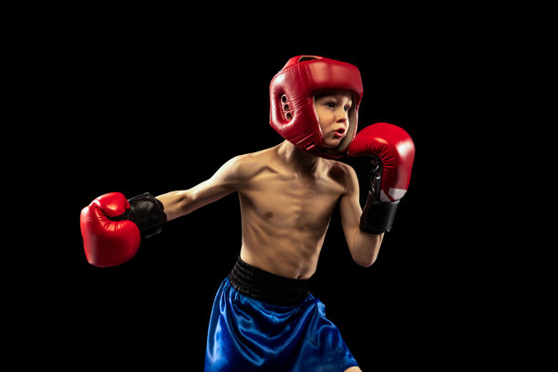 动态肖像运动的男孩，孩子在拳击手套和短裤练习孤立在黑暗的背景。运动、运动、学习、成就、积极的生活方式。素材图片