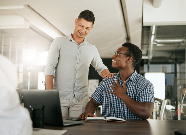 两个不同的商人坐在一张桌子上讨论笔记本电脑上的新项目。在现代办公室里，称赞同事工作出色，学习能力强图片下载
