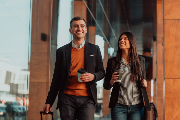 商务男士和商务女士在商务旅行中谈话，拿着行李，手里拿着新鲜的咖啡。经营理念图片下载