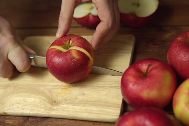 一只手拿着刀在砧板上切苹果。图片下载