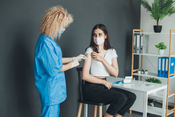 医院里，卷发医务人员为患者手臂接种疫苗，预防新冠病毒大流行，呵护健康图片下载