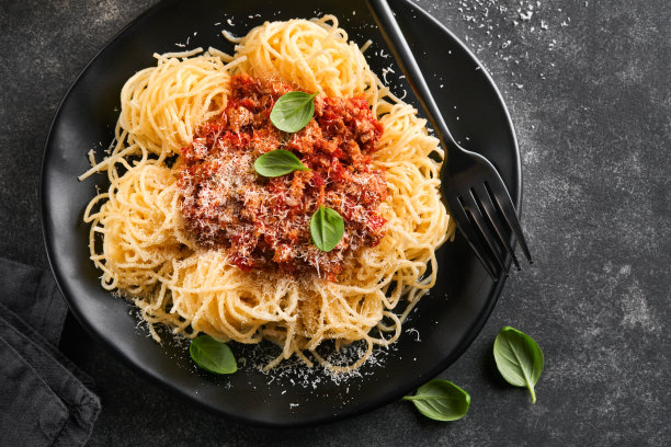 经典的意大利肉酱面。美味开胃的意大利意大利面配上肉酱，番茄酱，奶酪帕尔马和罗勒，黑色盘子，黑色石头或混凝土桌子背景。前视图。图片下载