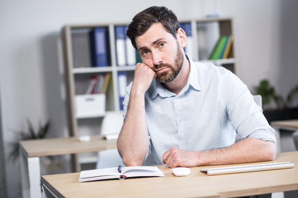 近距离的照片。心烦意乱，疲惫而有思想的年轻人，上班族，经理，自由职业者。他用手抱着头。坐在办公室的电脑桌前图片下载