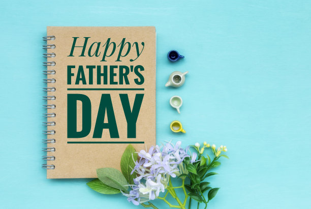 棕色笔记本上的父亲节快乐banner，配有迷你茶杯、茶壶和鲜花，蓝色背景留白图片下载