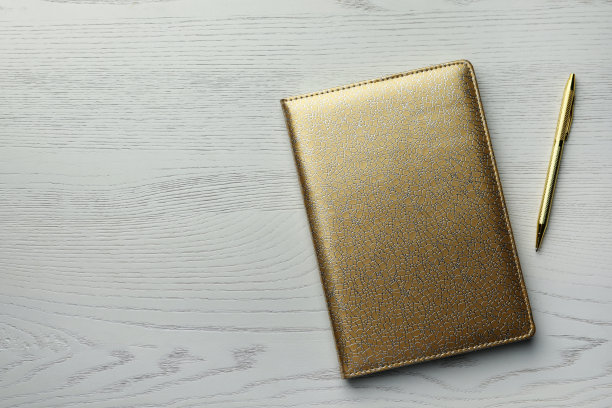 金色的记事本和笔放在白色的木桌上，平铺着。空间的文本图片下载