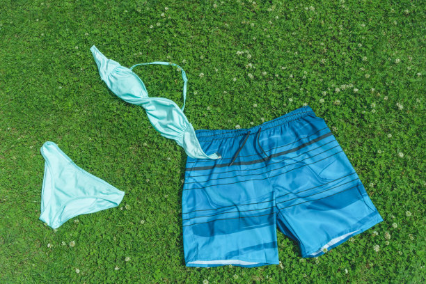女士泳装，男士蓝色泳裤在草地上。图片下载