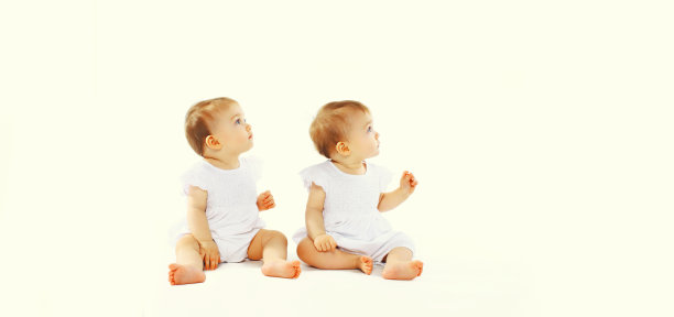 两个双胞胎宝宝坐在地板上，抬头看着白色的背景，空白的文案图片下载