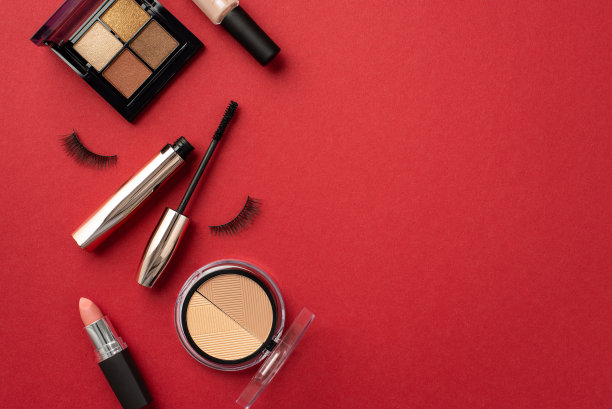 化妆美容的概念。顶视图照片的口红轮廓眼影调色板假睫毛睫毛膏和指甲油孤立的红色背景与copyspace图片下载