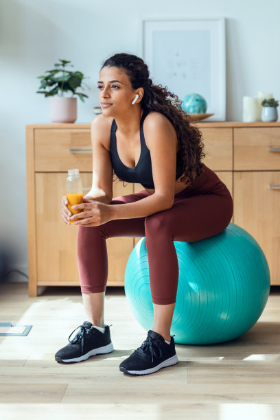 运动的年轻女子喝排毒果汁，同时在家里做运动与球。图片下载