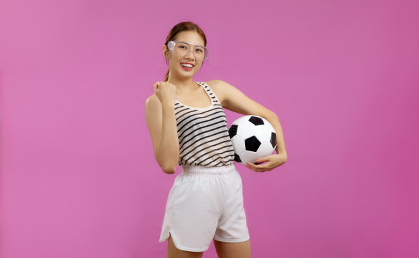 快乐的亚洲年轻女子在粉红色背景前拿着足球看着镜头图片下载