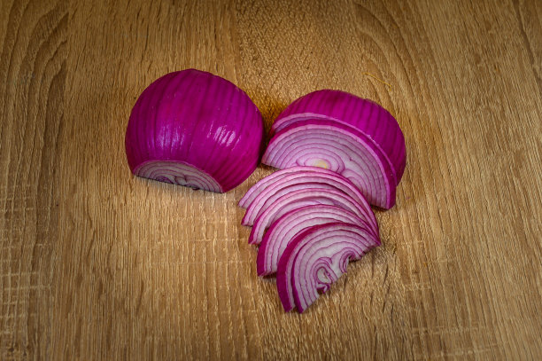 一个去皮的红洋葱，切成两半，一半是完整的，但是把皮倒着剥，露出紫色的层。另一半脸朝下切成条状。在一张榛木桌子上图片下载