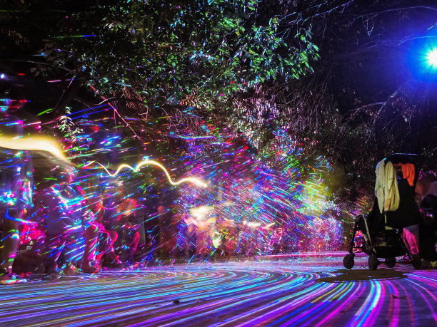 明亮的多色线条辉映在夜晚公园的小巷上，在散焦的行人背景上创造出一种图案。光影的游戏。长时间曝光的照片图片下载