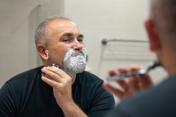 英俊的白发胡子男子剃掉他的胡子对着镜子。改变风格的概念图片下载